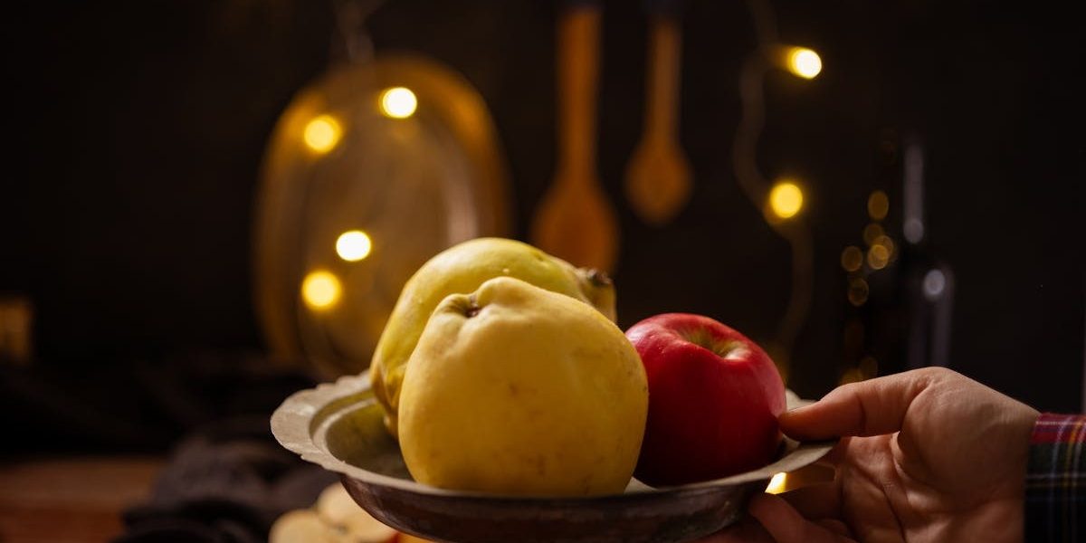A rustic composition featuring apples and quince illuminated by warm fairy lights indoors.