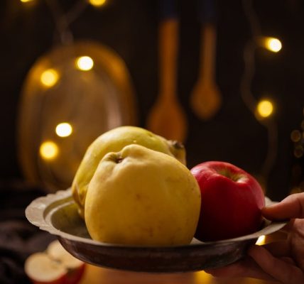 A rustic composition featuring apples and quince illuminated by warm fairy lights indoors.