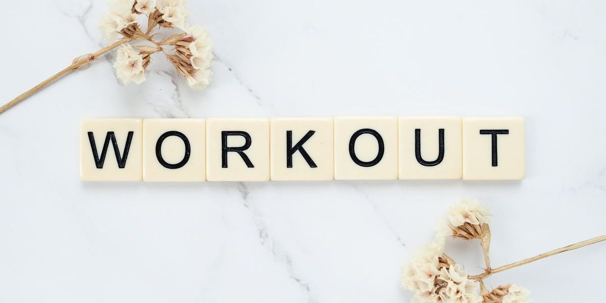 Letter tiles spelling 'WORKOUT' on marble with dried flowers, conveying fitness motivation.