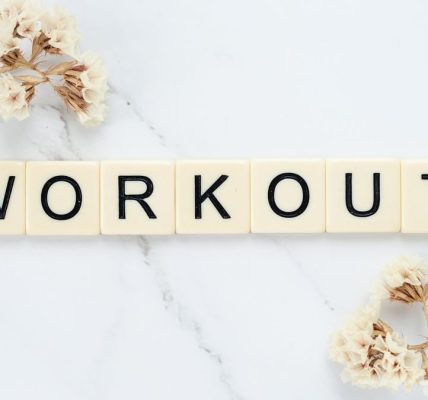 Letter tiles spelling 'WORKOUT' on marble with dried flowers, conveying fitness motivation.